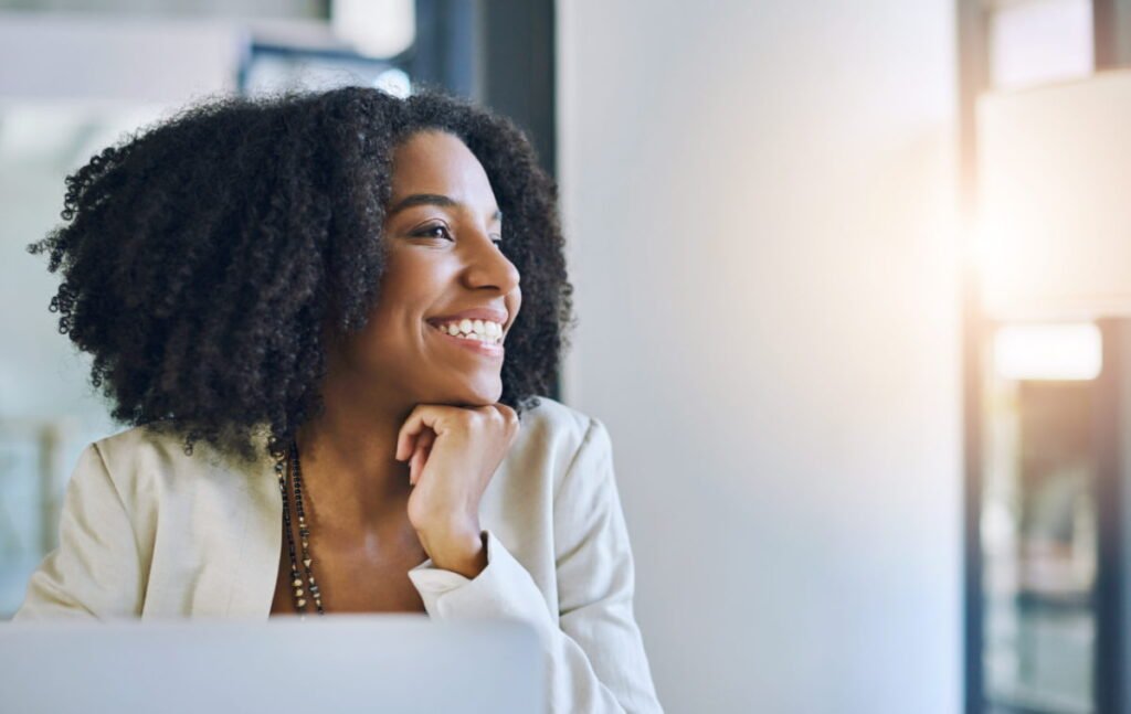 Shot of a young businesswoman smiling and looking out of a window in her office.