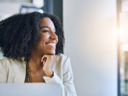 Shot of a young businesswoman smiling and looking out of a window in her office.